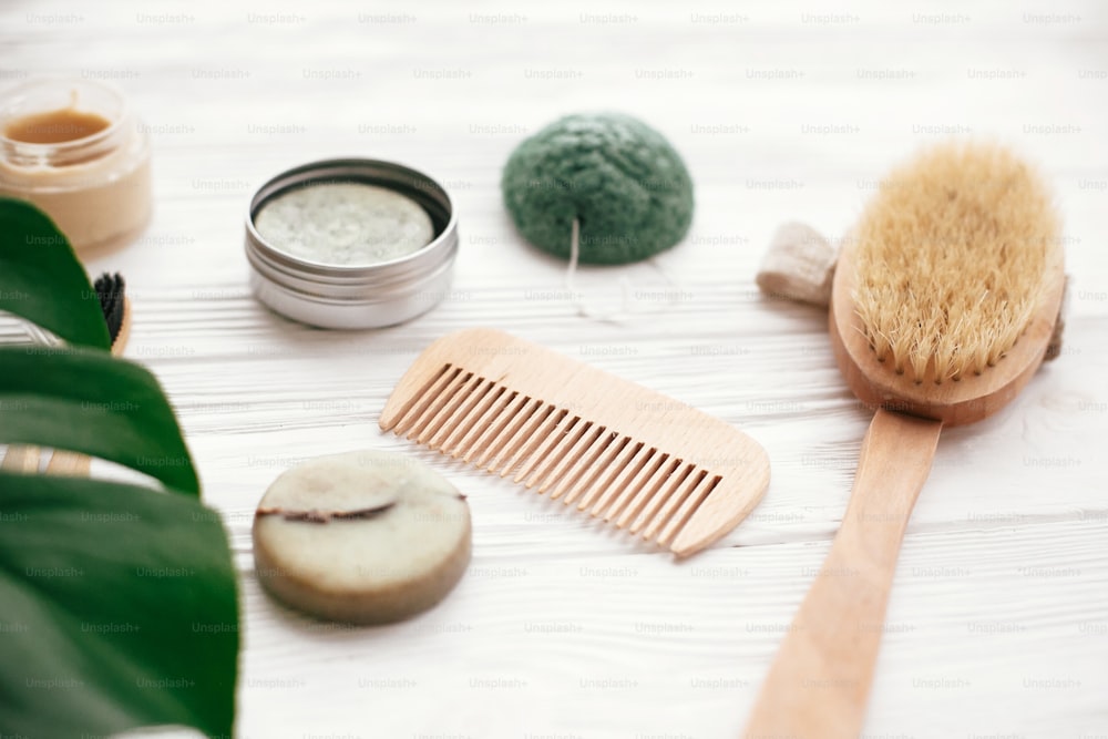 Zero waste solid shampoo bar, bamboo toothbrushes, wooden brush, natural deodorant and konjaku sponge on white wood with green monstera leaves. Eco  natural products plastic free