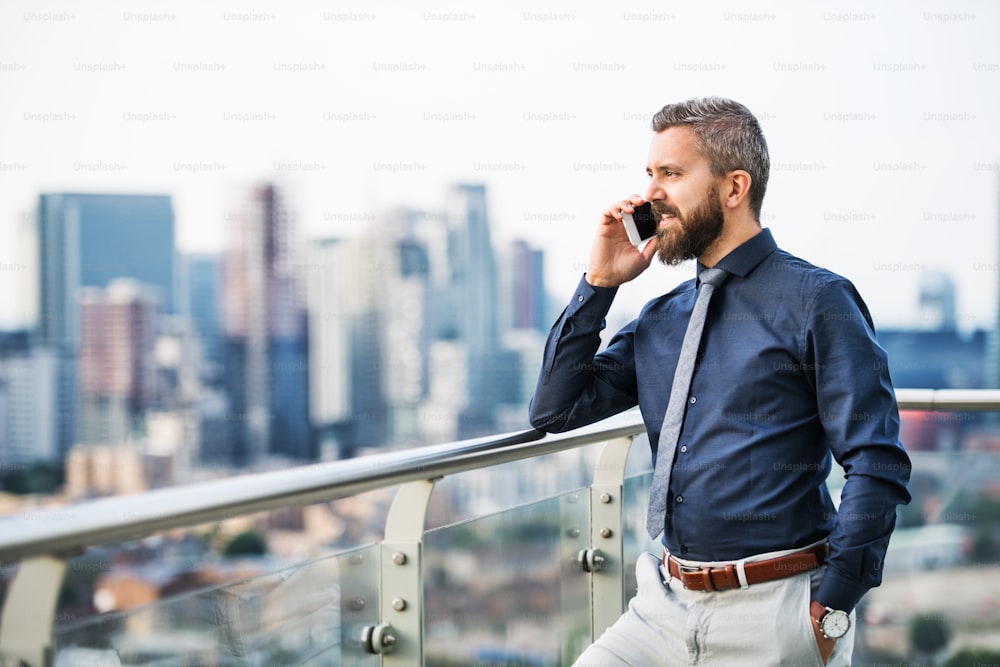 Un ritratto di uomo d'affari con smartphone in piedi contro il panorama panoramico di Londra, facendo una telefonata. Copia spazio.