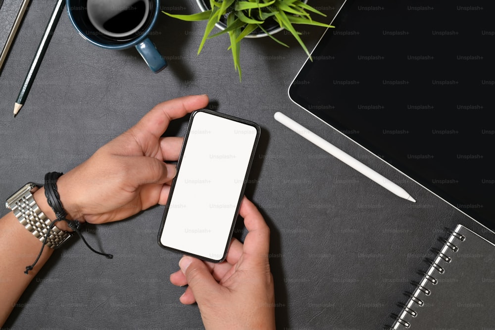 Teléfono inteligente moderno que sostiene la mano con pantalla en blanco aislada para maqueta en el escritorio de la oficina