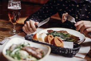 Mann isst köstliches saftiges Steak mit gegrilltem Kohl, Tomaten und Käse auf dem Tisch auf der Café-Terrasse in der Stadtstraße. Hände halten Gabel und Messer und probieren BBQ mit Gemüse im Restaurant