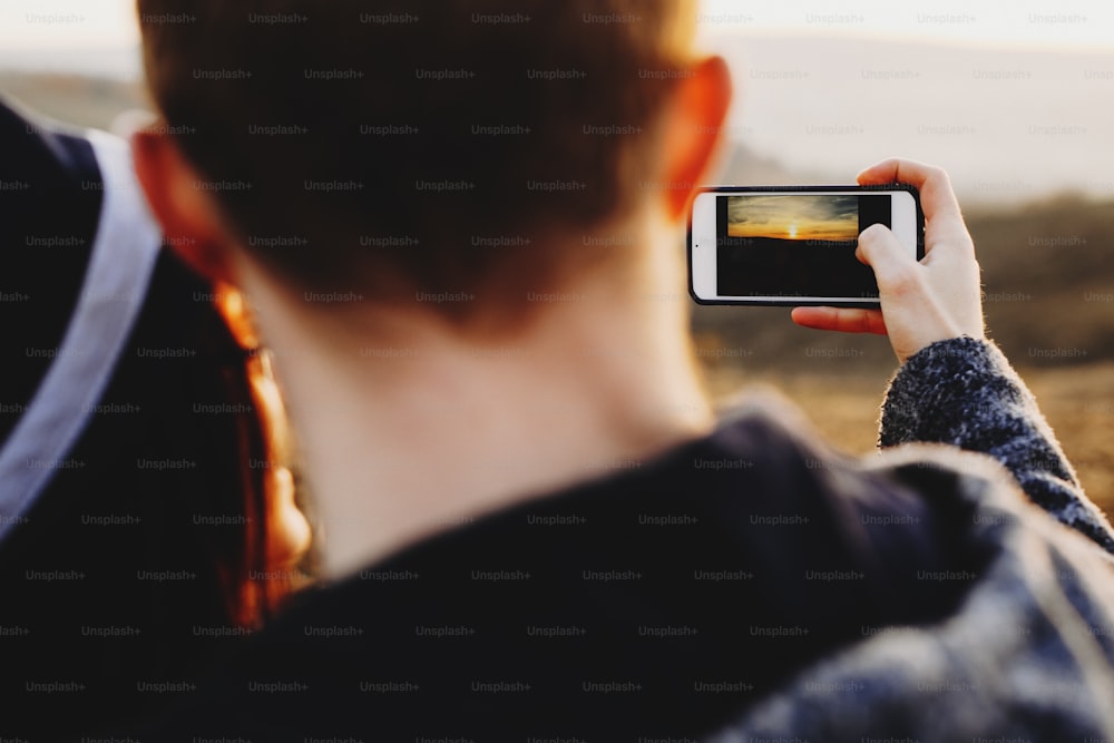 スマートフォンを使って田舎の素晴らしい夕日を撮影する匿名のカップルのクローズアップショット。日没の写真を撮るクロップカップル