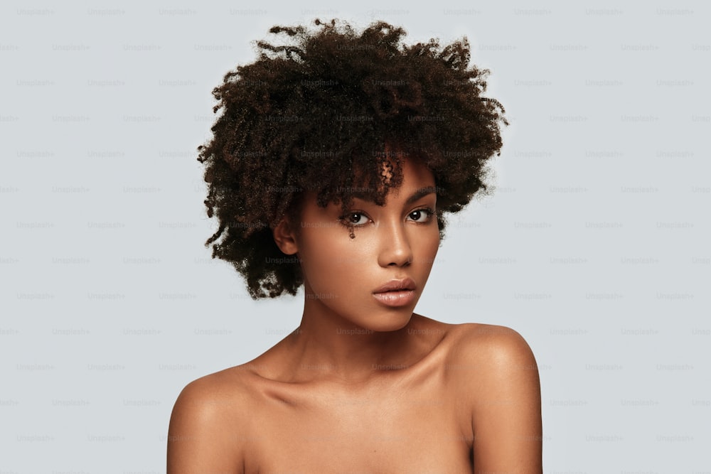 Attractive young African woman looking at camera while standing against grey background