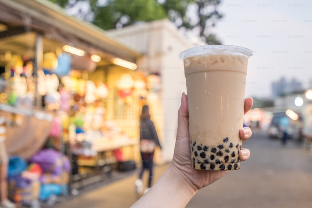 A young woman is holding a plastic cup of brown sugar bubble milk tea at a night market in Taiwan, Taiwan delicacy, close up.