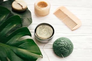 Natural eco friendly solid shampoo bar, wooden brush,  deodorant,soap, konjaku sponge on white wood with green monstera leaves. Zero waste products plastic free