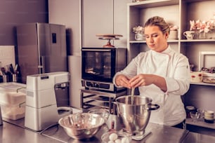 Sponge cake preparation. Nice pastry chef adding eggs to the bowl while preparing the cake