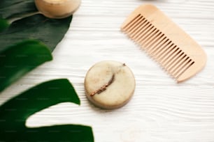 Natural eco friendly solid shampoo bar, wooden brush,  conditioner,soap, deodorant cream on white wood with green monstera leaves.  Eco products plastic free. Zero waste concept.