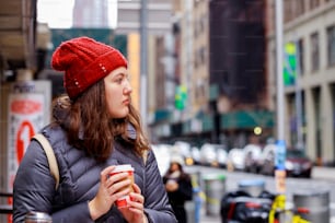 Menina adolescente jovem feliz que bebe café da xícara de papel na rua da cidade