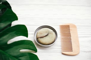 Natural eco friendly solid shampoo bar, wooden brush,  green  conditioner, soap on white wood with green monstera leaves.  Eco products plastic free. Zero waste concept.