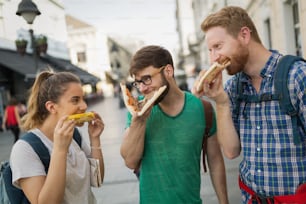 Happy people eating fast food in city while travelling with backpacks