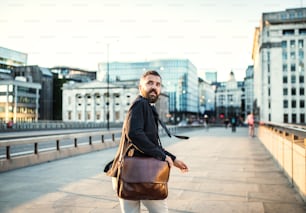 Una vista posteriore di un uomo d'affari hipster con una borsa che corre per strada in città, guardando indietro.
