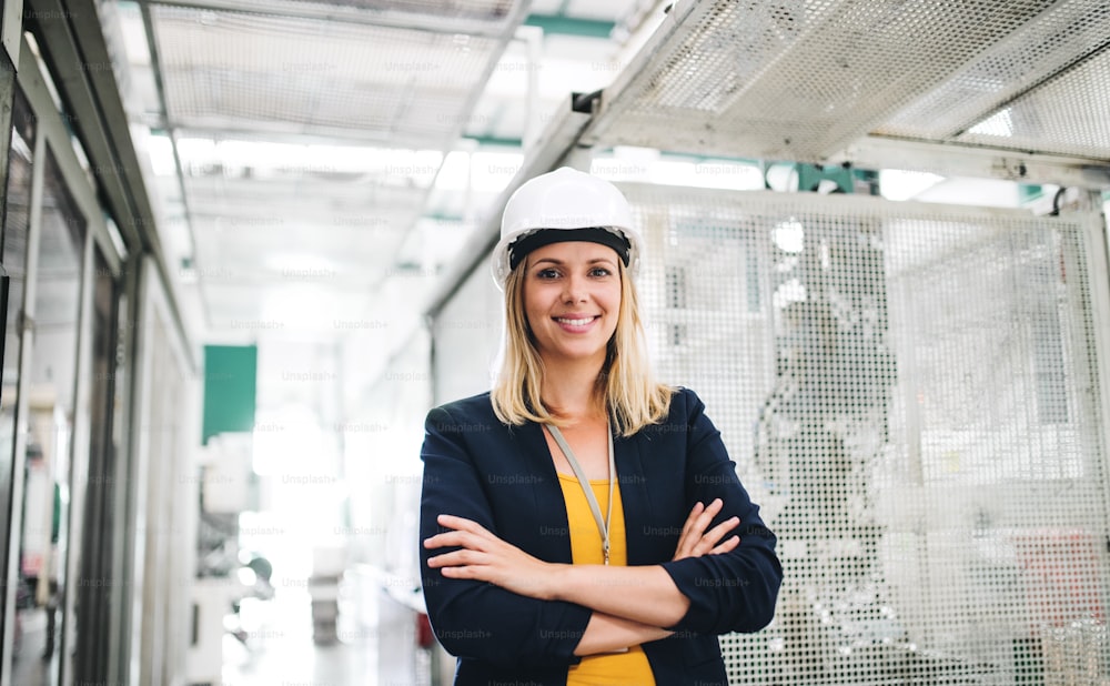 A portrait of a young industrial woman engineer standing in a factory, arms crossed.