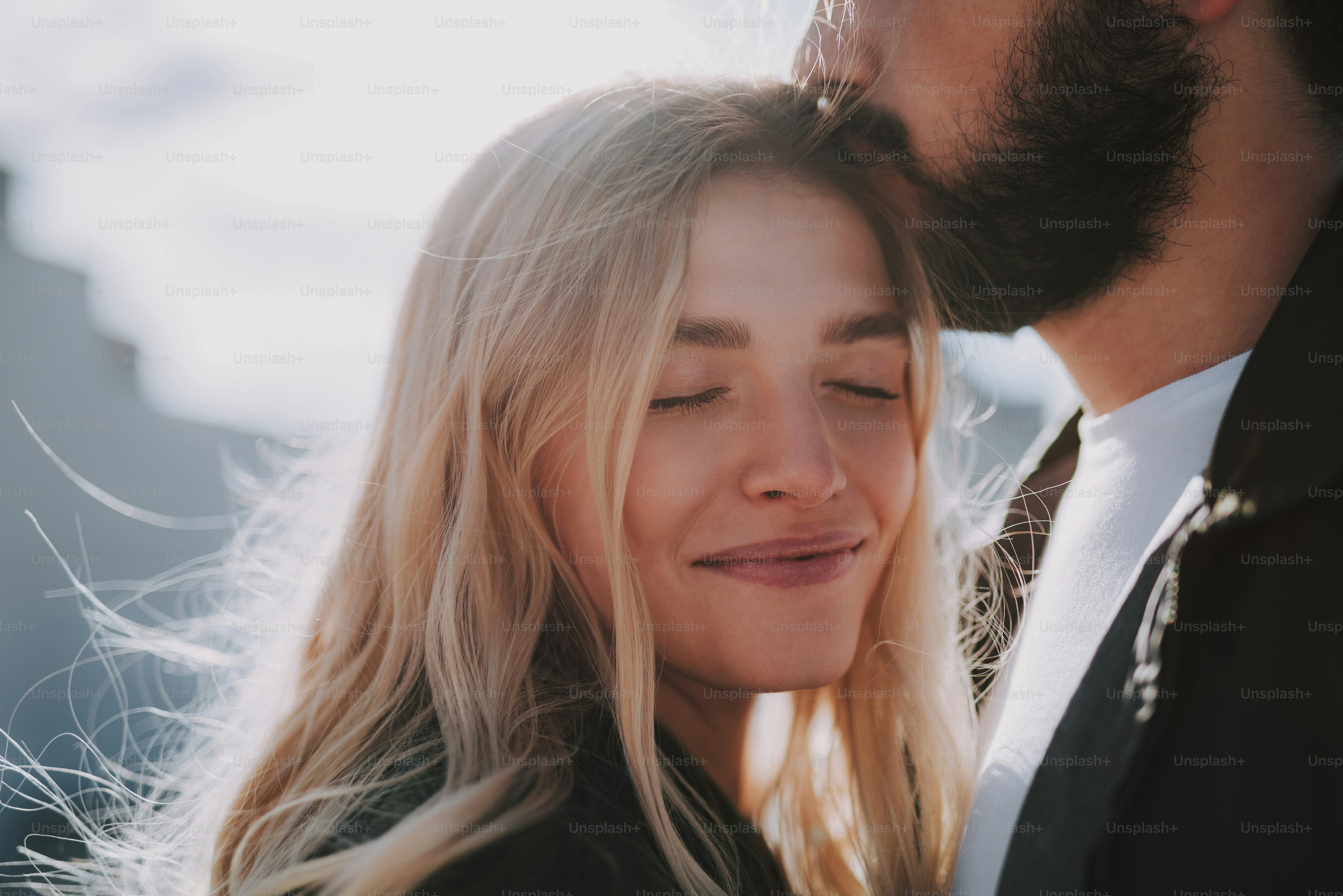 Momento romantico. Ritratto ravvicinato di affascinante ragazza bionda che chiude gli occhi e sorride mentre l'uomo barbuto la bacia