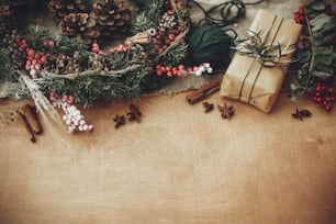 Buon Natale, concetto Eco. Elegante confezione regalo rustica con ramo verde e rami di abete, bacche, anice, pigne, cannella su sfondo rustico in legno. Semplice eco presente. Spazio per il testo