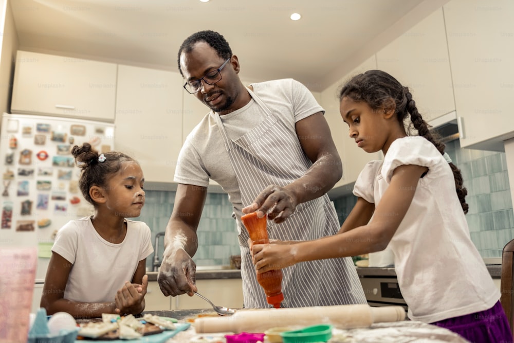 피자 요리. 안경을 쓴 검은 머리 아버지와 저녁 식사를 위해 피자를 요리하는 귀여운 딸들