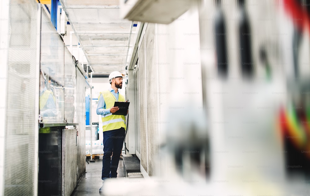 A portrait of a mature industrial man engineer with clipboard in a factory, working. Copy space.