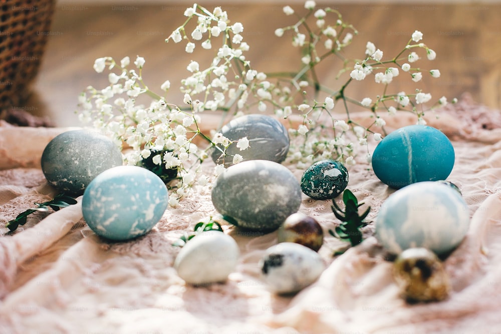 Elegantes huevos de pascua con flores de primavera sobre tela rústica sobre madera a la luz del sol. Huevos de pascua modernos pintados con tinte natural en color mármol azul, gris. Felices Pascuas, tarjeta de felicitación