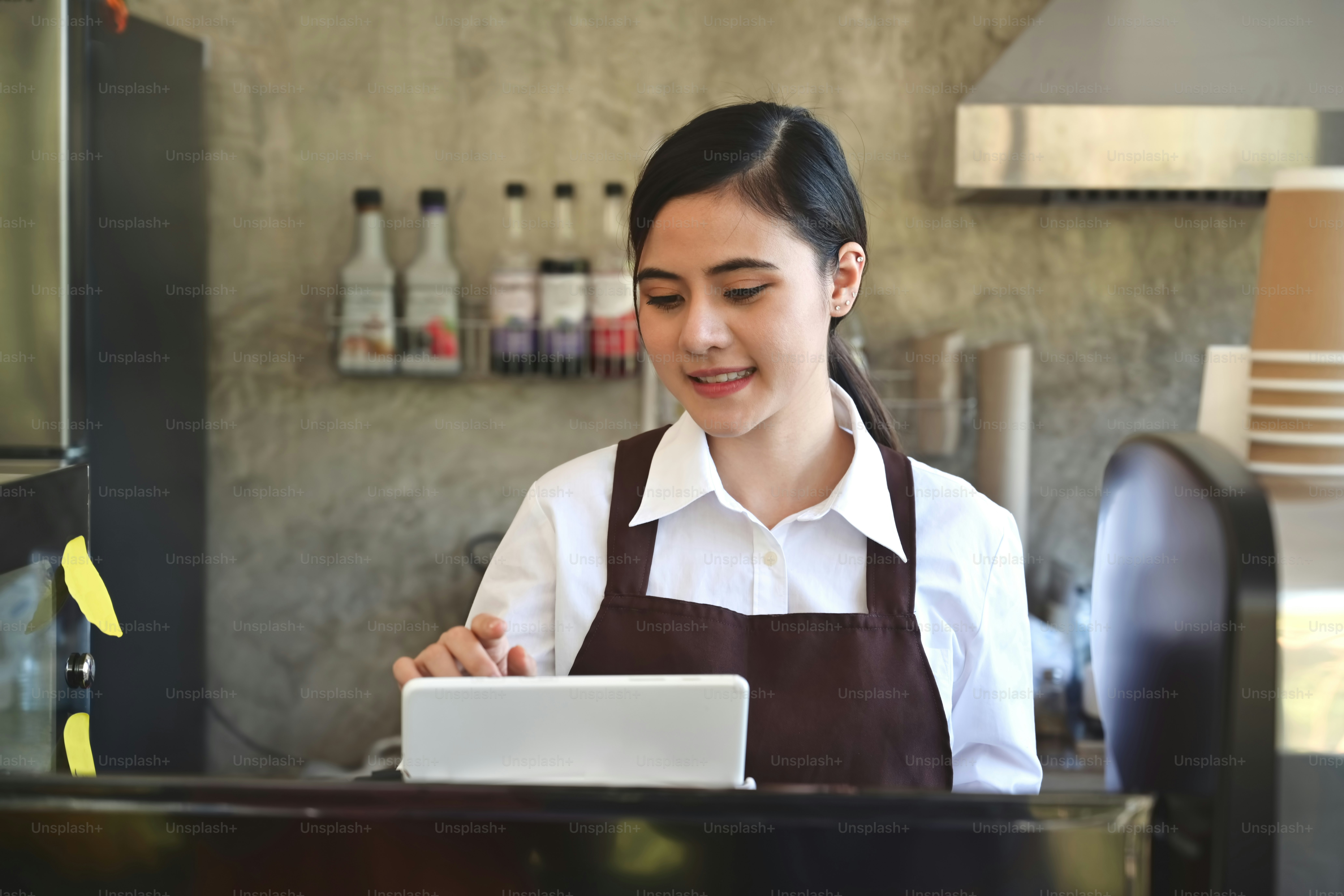 Mujeres asiáticas Barista sonriendo y usando tableta para tomar el pedido en el mostrador de la cafetería