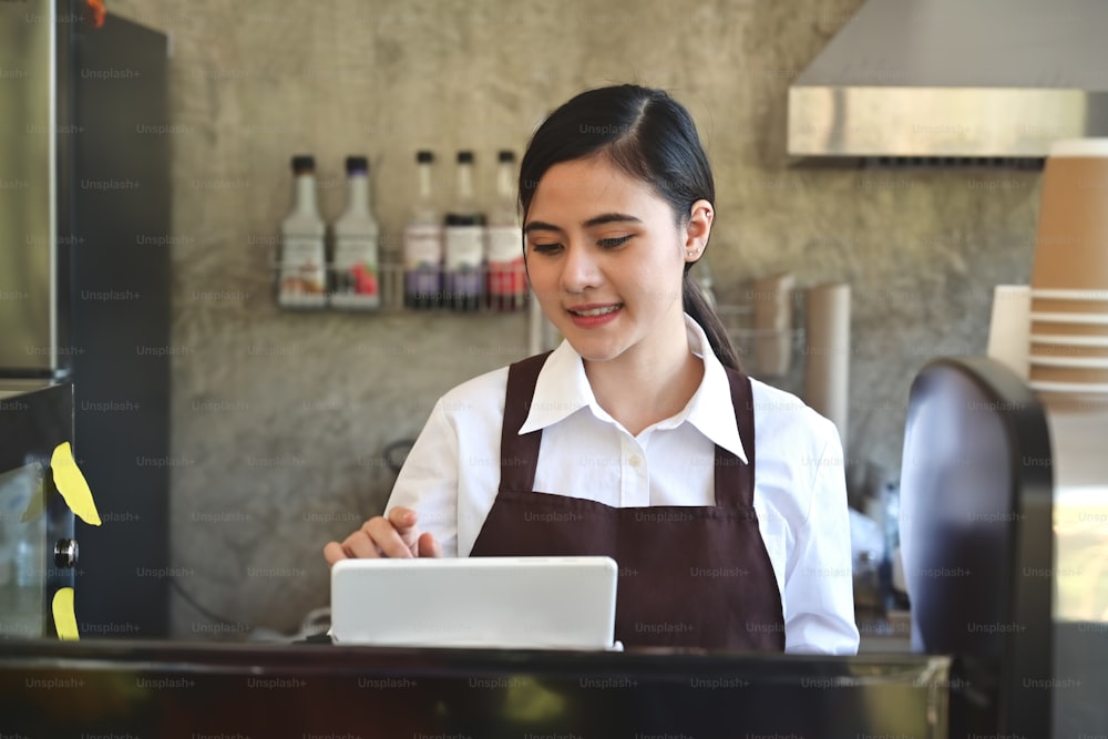 Asian women Barista smiling and using tablet for take order in coffee shop counter