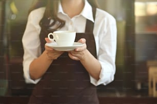 Barista in apron holding coffee in coffee shop