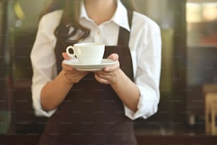 Barista con delantal sosteniendo café en cafetería