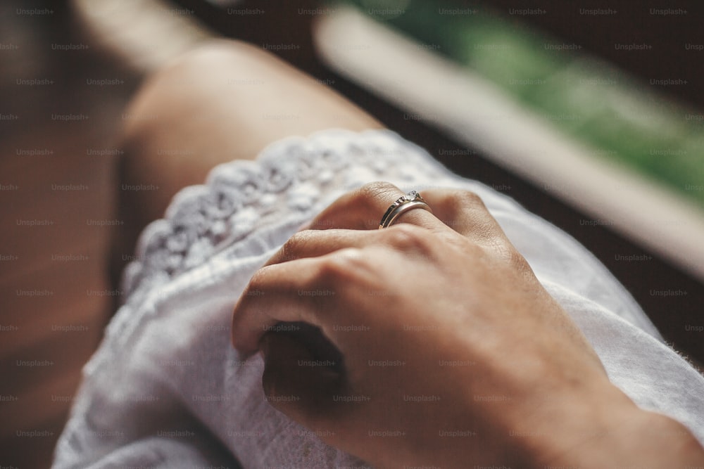 Hand with engagement ring on girl white bohemian dress on wooden porch in summer mountains. Silver ring with crystal. Girl relaxing in woods. Just engage