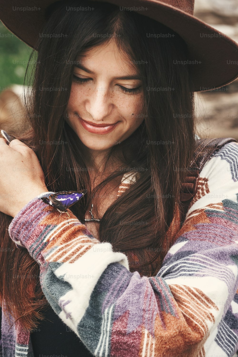 여름 산에서 보라색 황제 나비를 손에 들고 모자를 쓴 세련된 힙스터 소녀. 나비와 함께 야외를 탐험하는 젊은 여성 여행자. 아파투라 아이리스