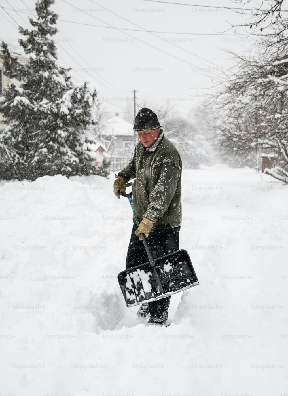 Remoción de nieve invernal. Un hombre con una pala limpia el patio y el camino de entrada de nieve durante la nieve intensa