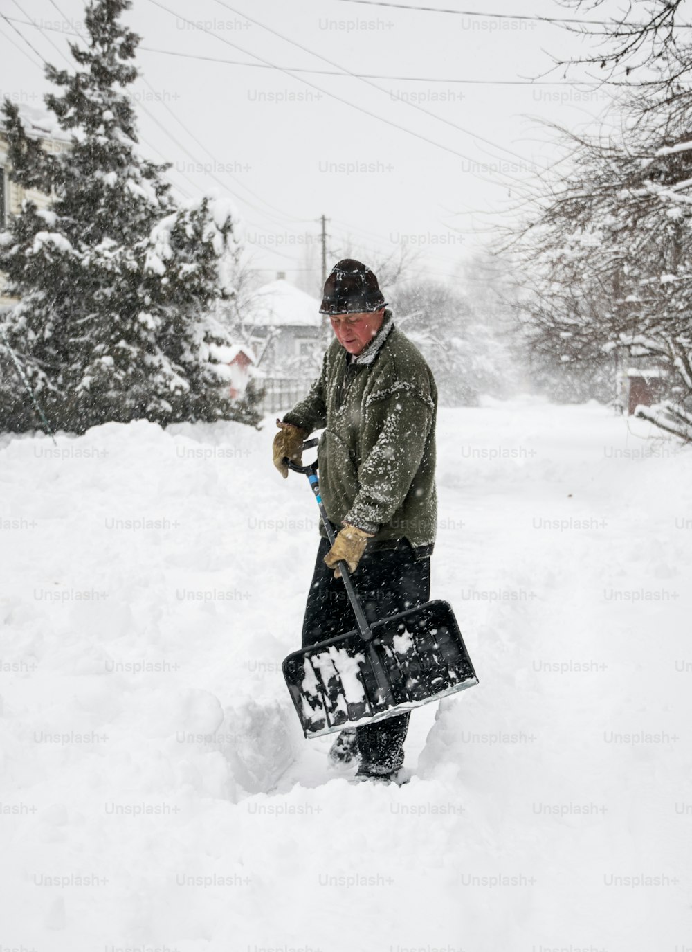 Schneeräumung im Winter. Ein Mann mit einer Schaufel räumt den Hof und die Einfahrt von Schnee bei starkem Schneefall