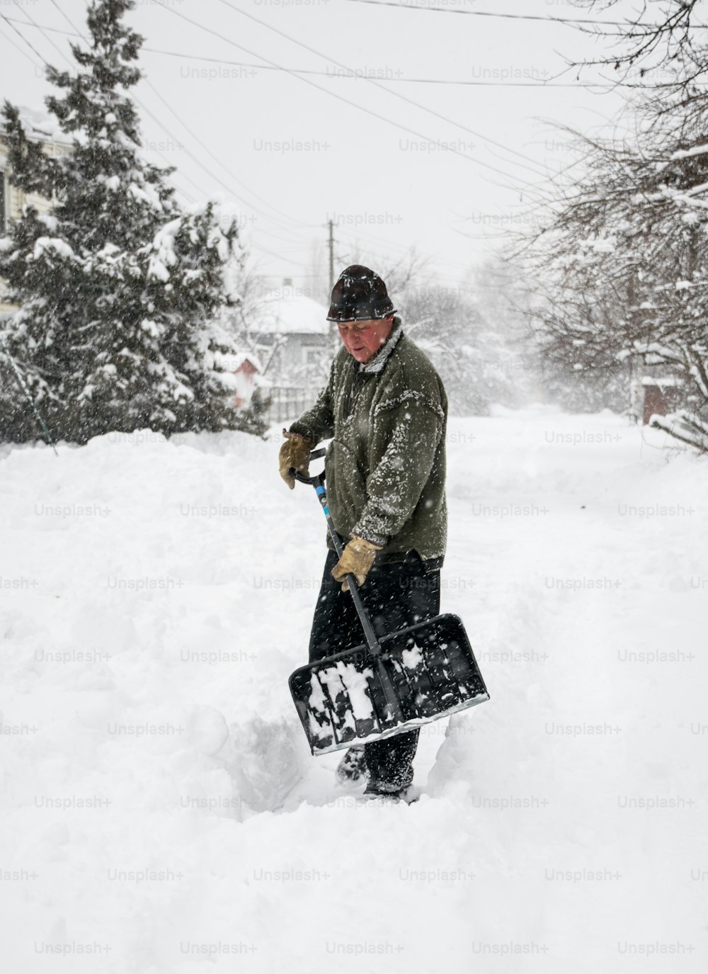 Winter snow removal. A man with a shovel clears the yard and driveway from snow during heavy snow
