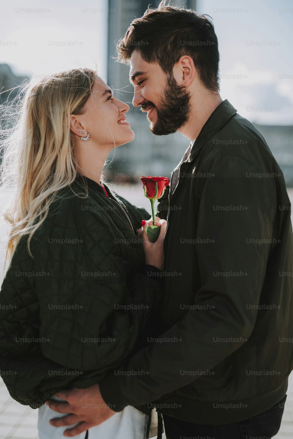 Side view waist up portrait of charming girl with red rose looking at bearded man and smiling