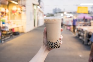 A young woman is holding a plastic cup of brown sugar bubble milk tea at a night market in Taiwan, Taiwan delicacy, close up.