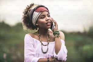 Concept of hippie lifestyle. Close up portrait of smiling afro-american female staying on grass road background and talking by mobile phone