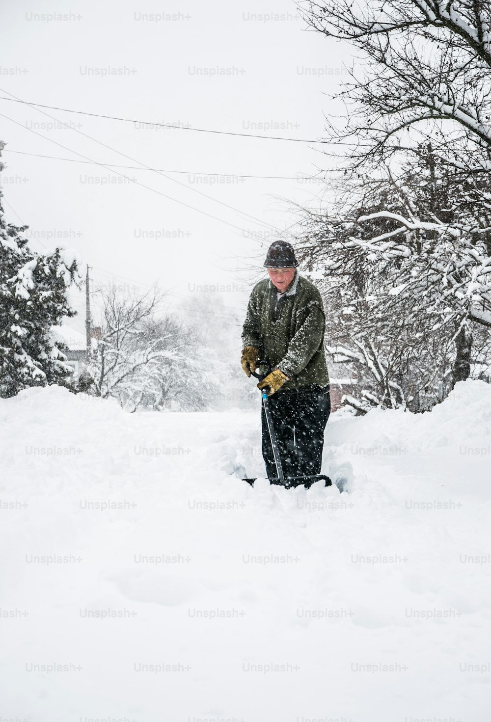 Remoción de nieve invernal. Un hombre con una pala limpia el patio y el camino de entrada de nieve durante la nieve intensa