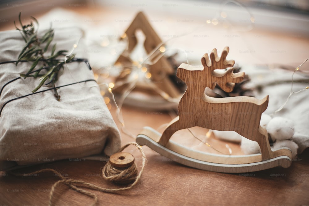Cadeau rustique de Noël élégant enveloppé dans un tissu de lin avec une branche verte sur une table en bois avec des pommes de pin, des rennes, de la ficelle, des lumières. Simple eco présente sans plastique. Des vacances zéro déchet.