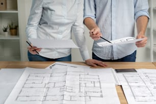 Cropped photo group of two person in formalwear shirt stand at the table in light loft interior workplace make modern renovation look at blank on room pointer on structure document by pencil