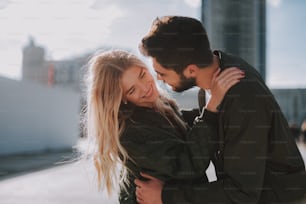 Portrait of handsome bearded man embracing his charming girlfriend and trying to kiss her. Lady looking away and smiling