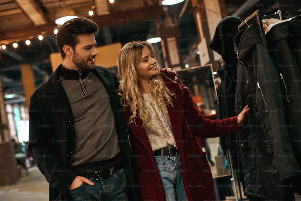 We should buy this stuff. Happy young joyful couple choosing handmade eco fur coat at small street market. Autumn season, blond haired woman with her boyfriend are in street market