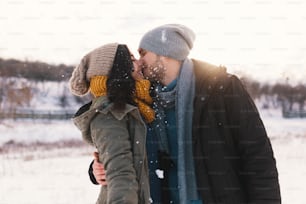 幸せな女性と男性、キスをし、抱きしめ、お互いを抱きしめ合う時間、雪、人生、冬。スタイリッシュなウールの帽子とスカーフを身に着けた素晴らしい若いカップルの肖像画。