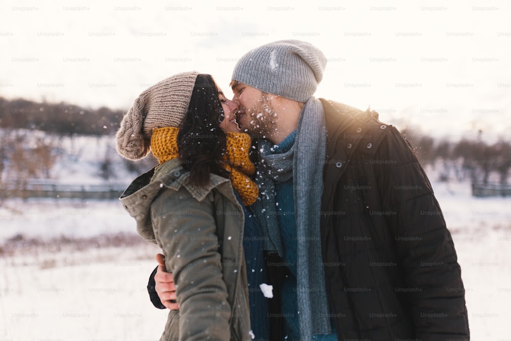 Happy woman and man, kissing, and huging, spending time together enjowing eachother, snow, life, winter. Portrait wonderful young couple wearing stylish wool hats and scarfs.