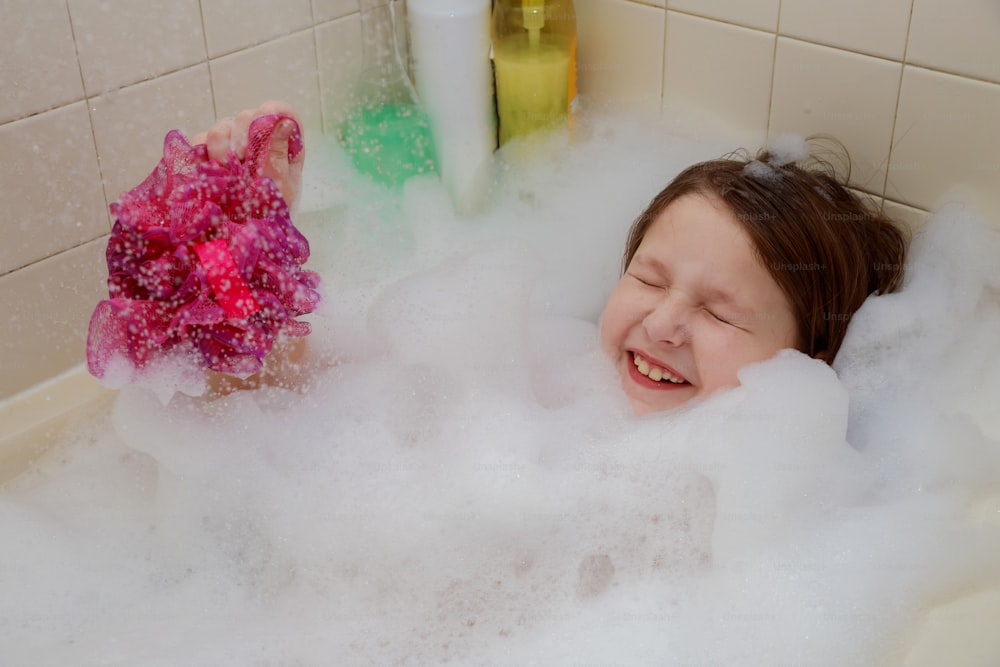Baby little girl sitting up to their necks in bubbles in the bath have fun blowing bubbles their cupped hands