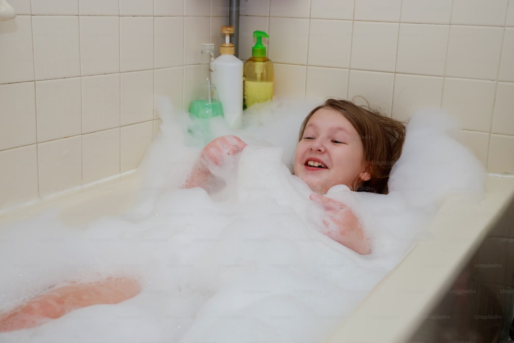 little child is washing her hair in bath playing with foam bubbles