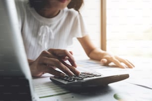 Primo piano Donna d'affari che utilizza calcolatrice e computer portatile per fare finanza matematica su scrivania di legno in ufficio e business sfondo di lavoro, tasse, contabilità, statistiche e concetto di ricerca analitica