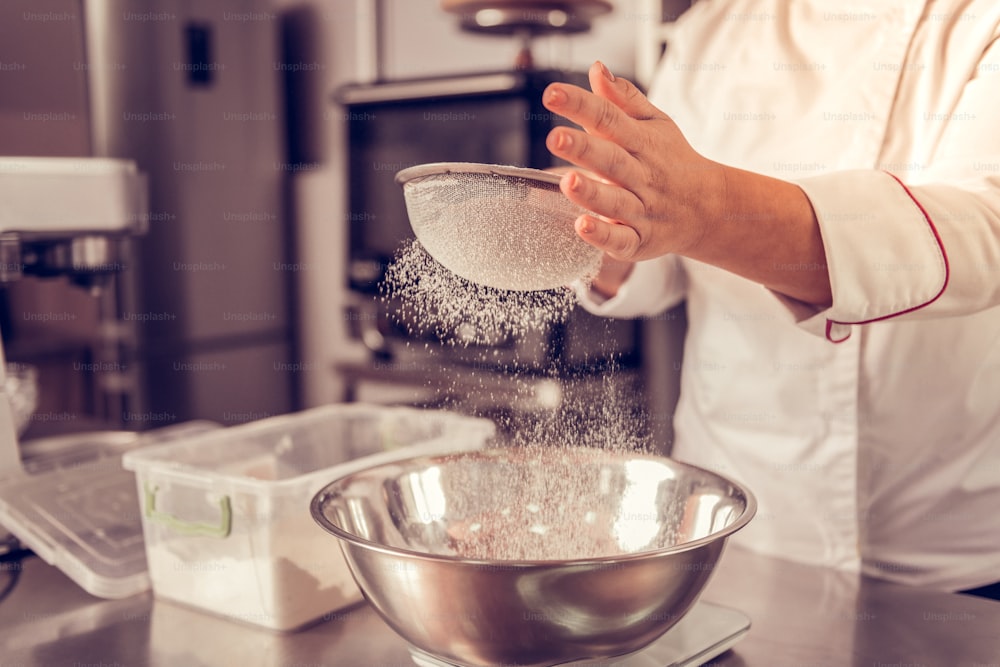 Kitchen equipment. Close up of a flout sifter being in female hands during the process of food preparation