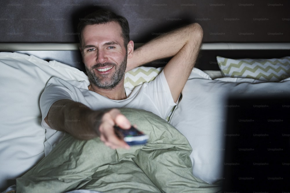 Homme allongé sur le lit et regardant la télévision la nuit
