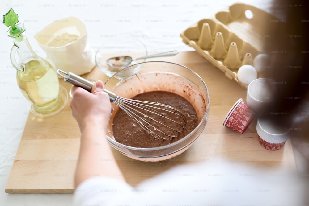 クリスマスチョコレートマフィンを調理します。ブラウニー、カップケーキ、パンケーキの材料を混ぜる。準備する女性の手