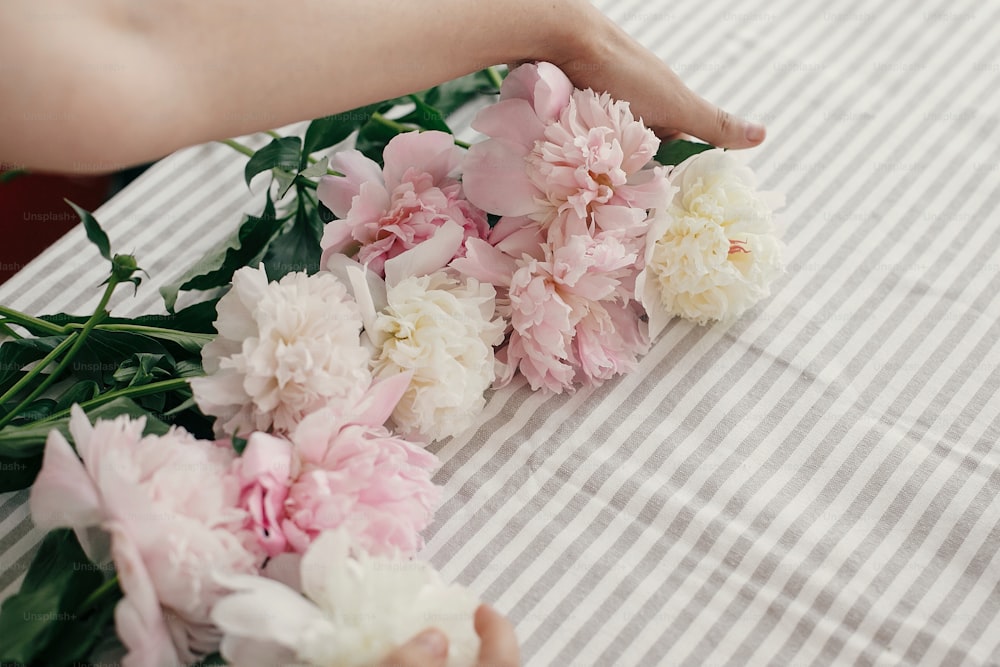 Beautiful peonies in girl hands. Florist arranging peony flowers on rustic table. Happy mothers day. Valentines day. Aroma scent concept. International Womens Day.