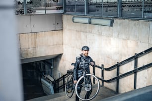 Corriere maschio che consegna pacchi in città, portando la bicicletta su per le scale. Copia spazio.