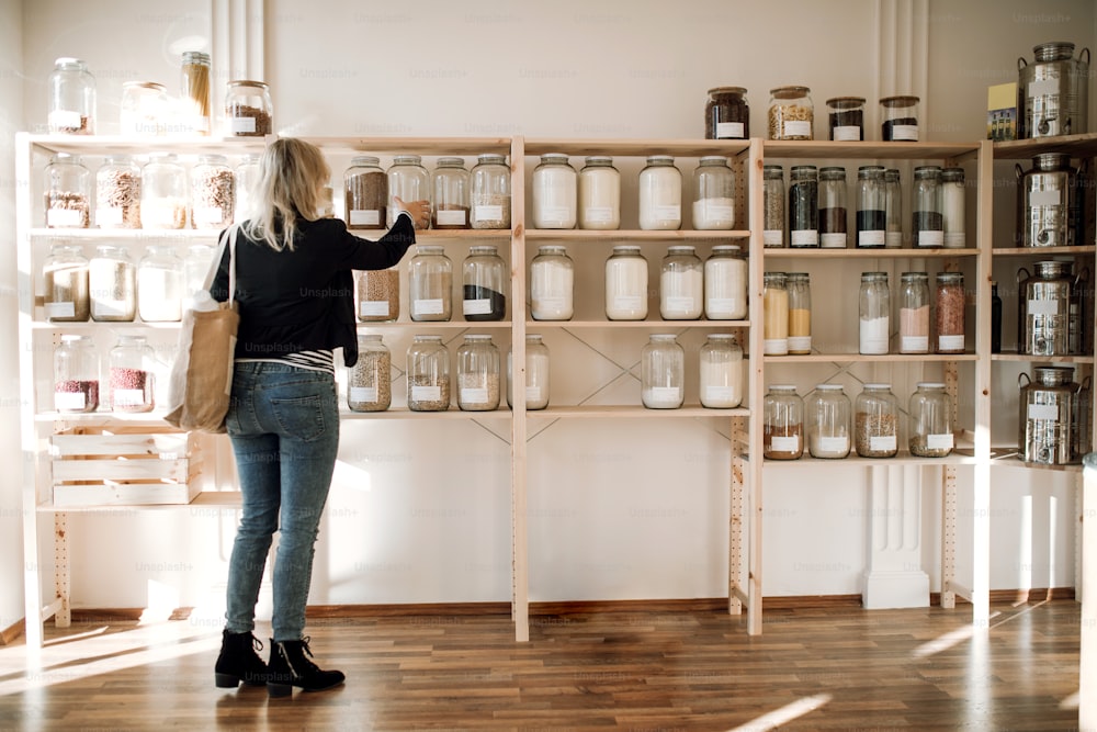 A rear view of attractive young happy woman buying groceries in zero waste shop. Copy space.
