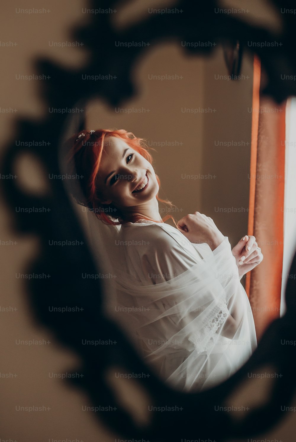 happy stylish bride in silk robe looking in mirror on the wall and smiling.  rustic wedding morning preparation. portrait reflection of young woman. space for text. luxury bride