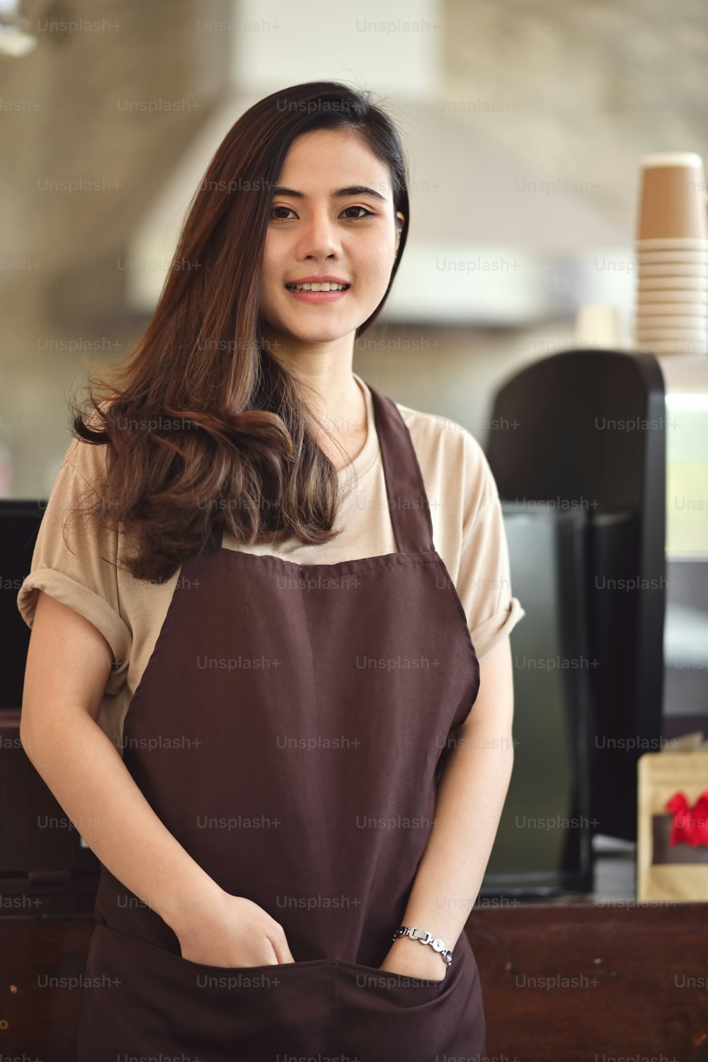 Portrait of attractive Asian barista woman standing at front of coffee bar counter.